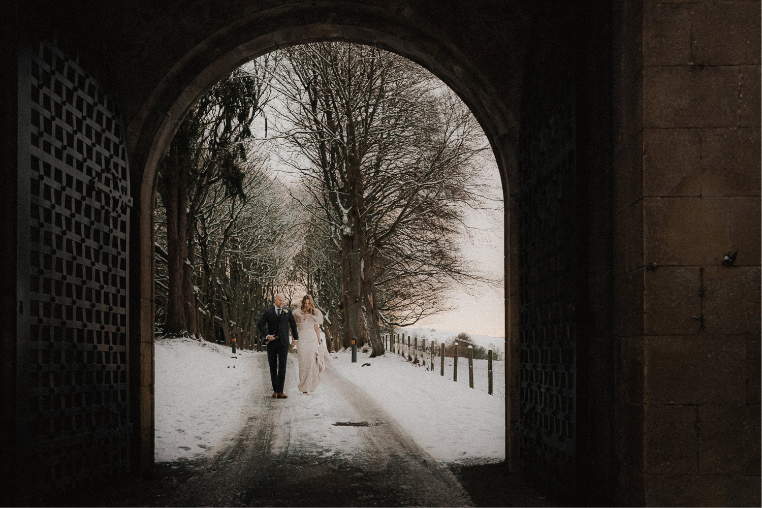 A wedding couple strolling through a snowy archway.