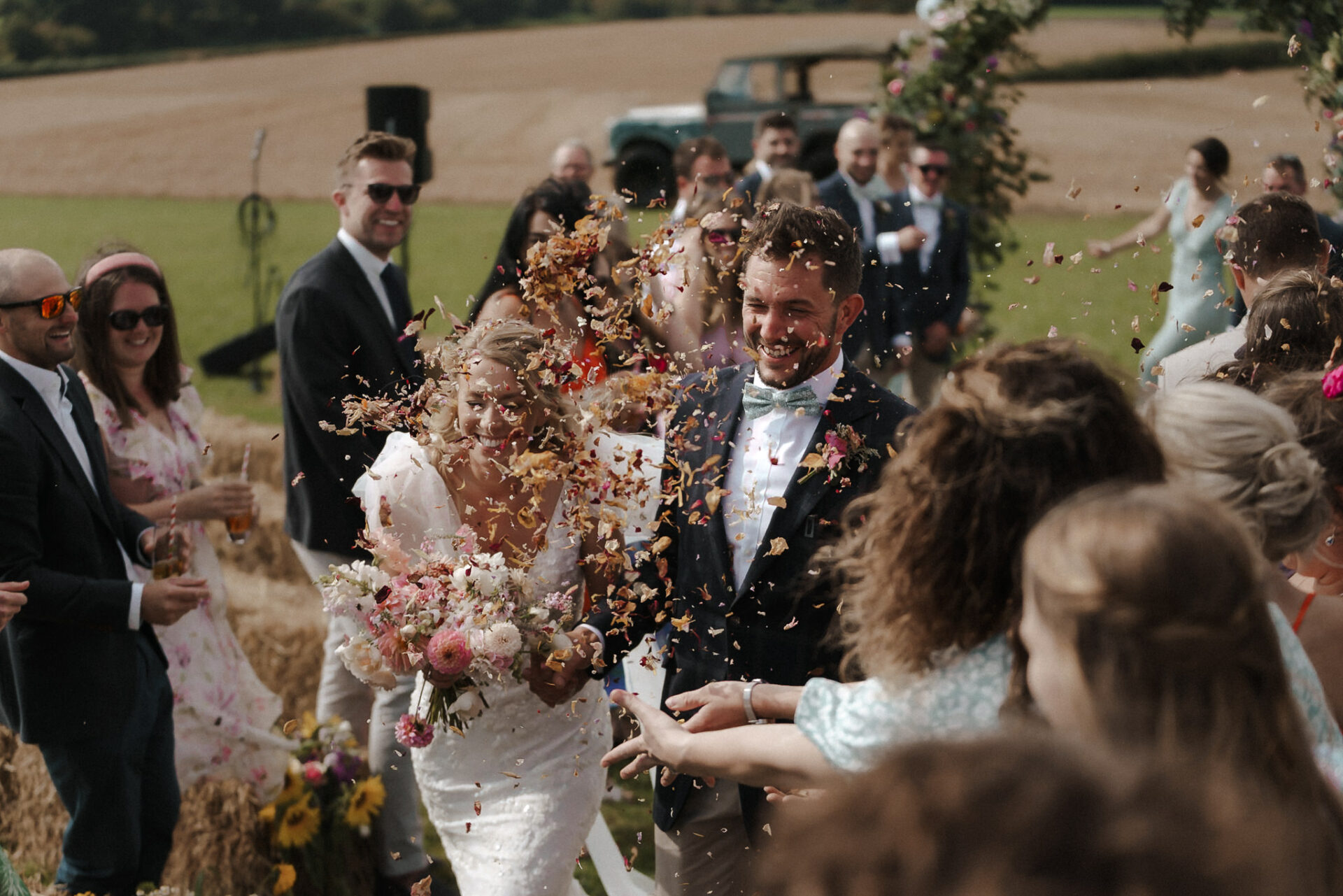 A joyful bride and groom walking through a shower of confetti with guests looking on.