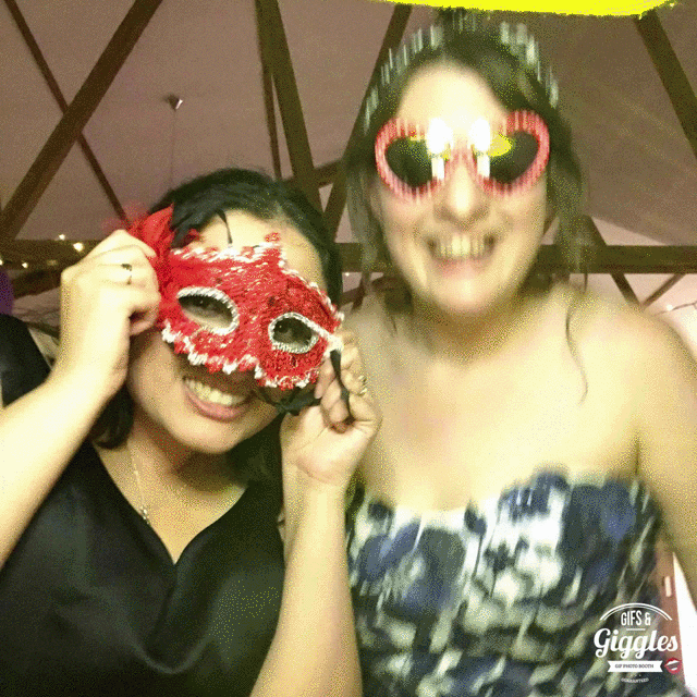 Two women posing for a wedding photo with masks on their faces at a gifbooth.