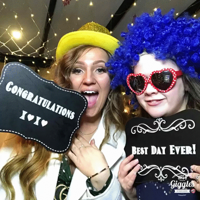 Two women holding up signs with the words best day ever at a wedding photo booth.