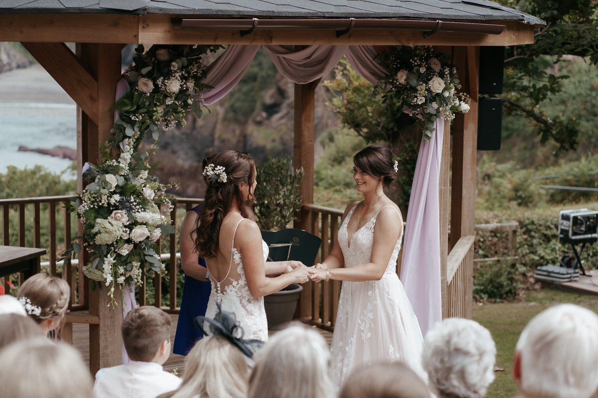 Two brides exchanging vows in front of a gazebo.