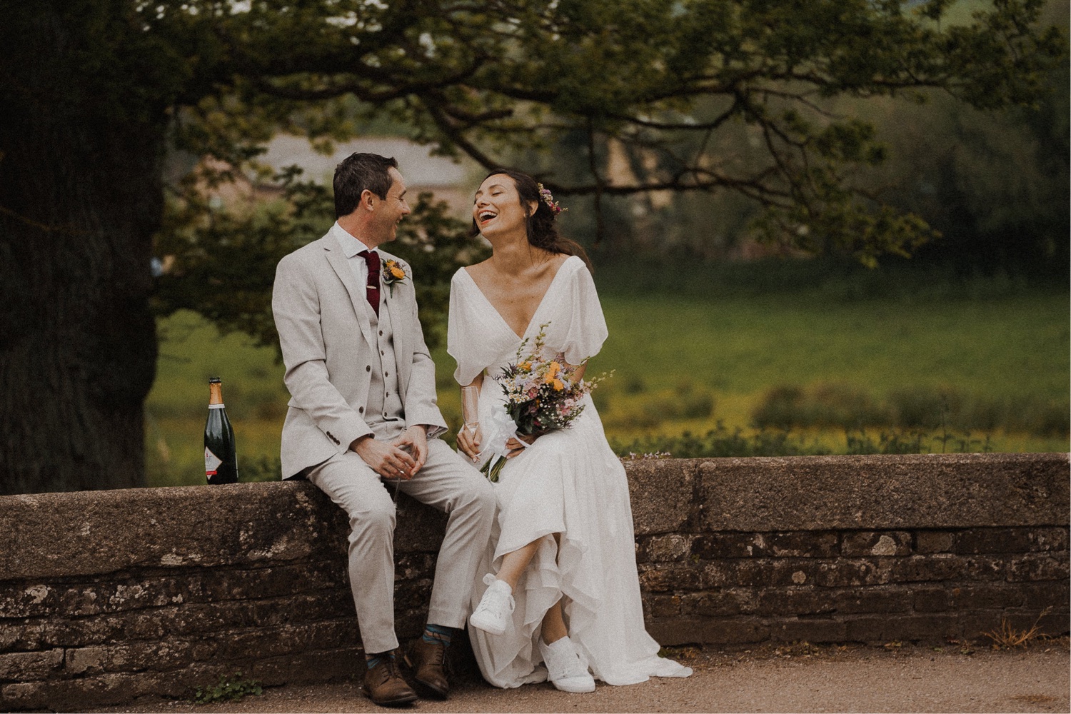 A couple in wedding photographs sitting on a stone wall.