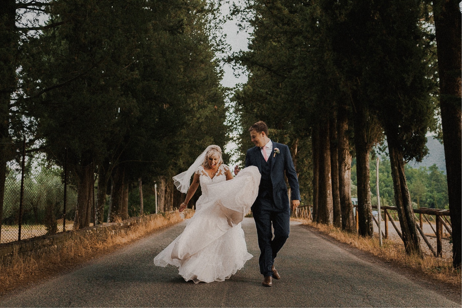 A newlywed couple strolling along a beautiful tree lined path in Tuscany.