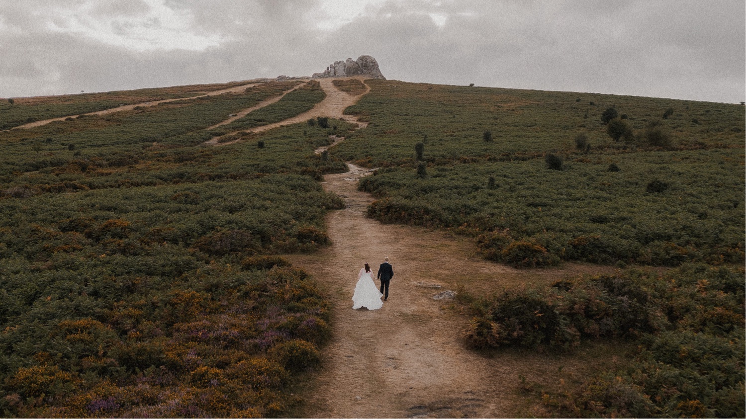 A couple posing for wedding photographs as they walk down a path in a forest.