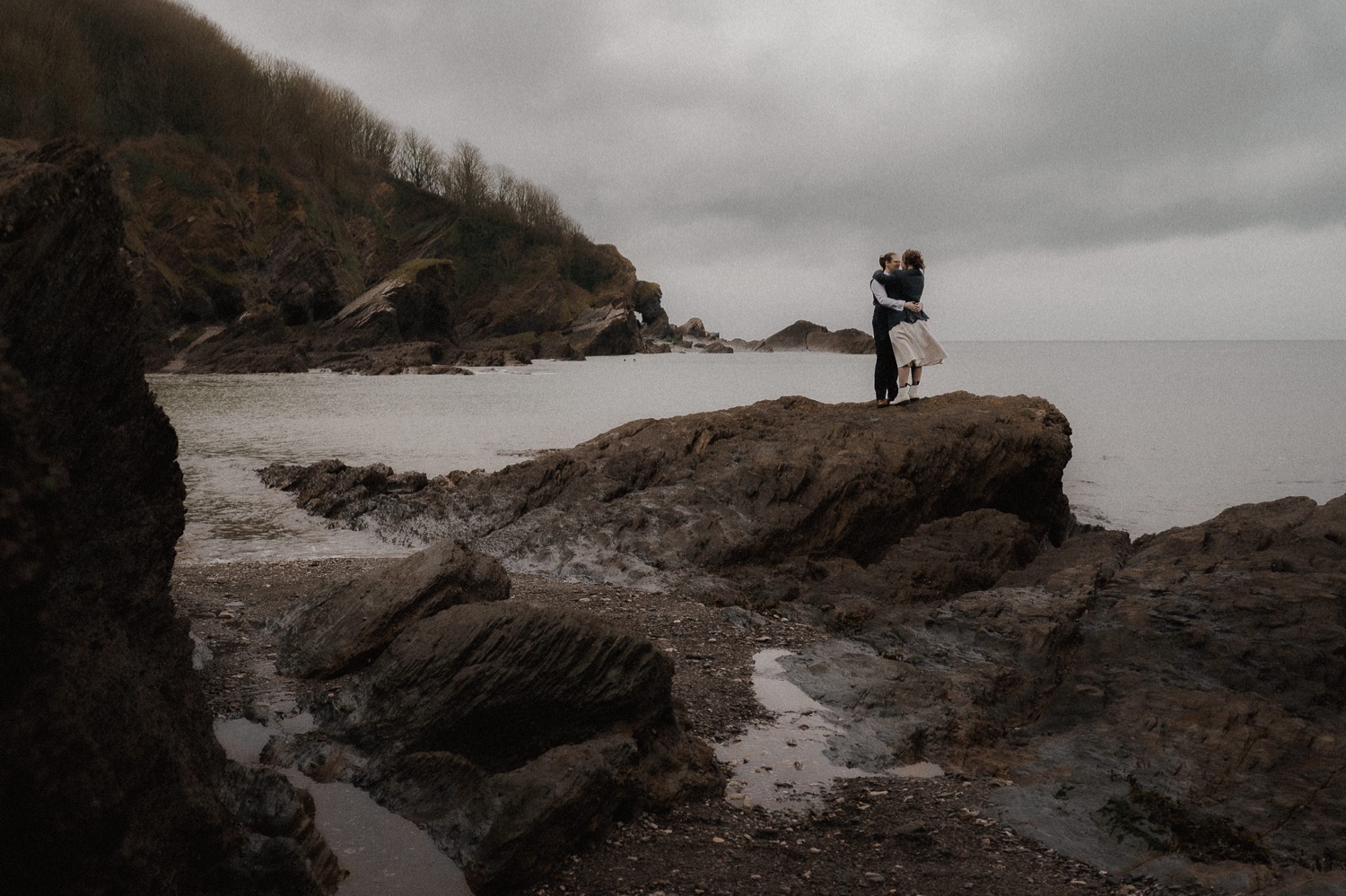 A couple standing on rocks near the ocean.