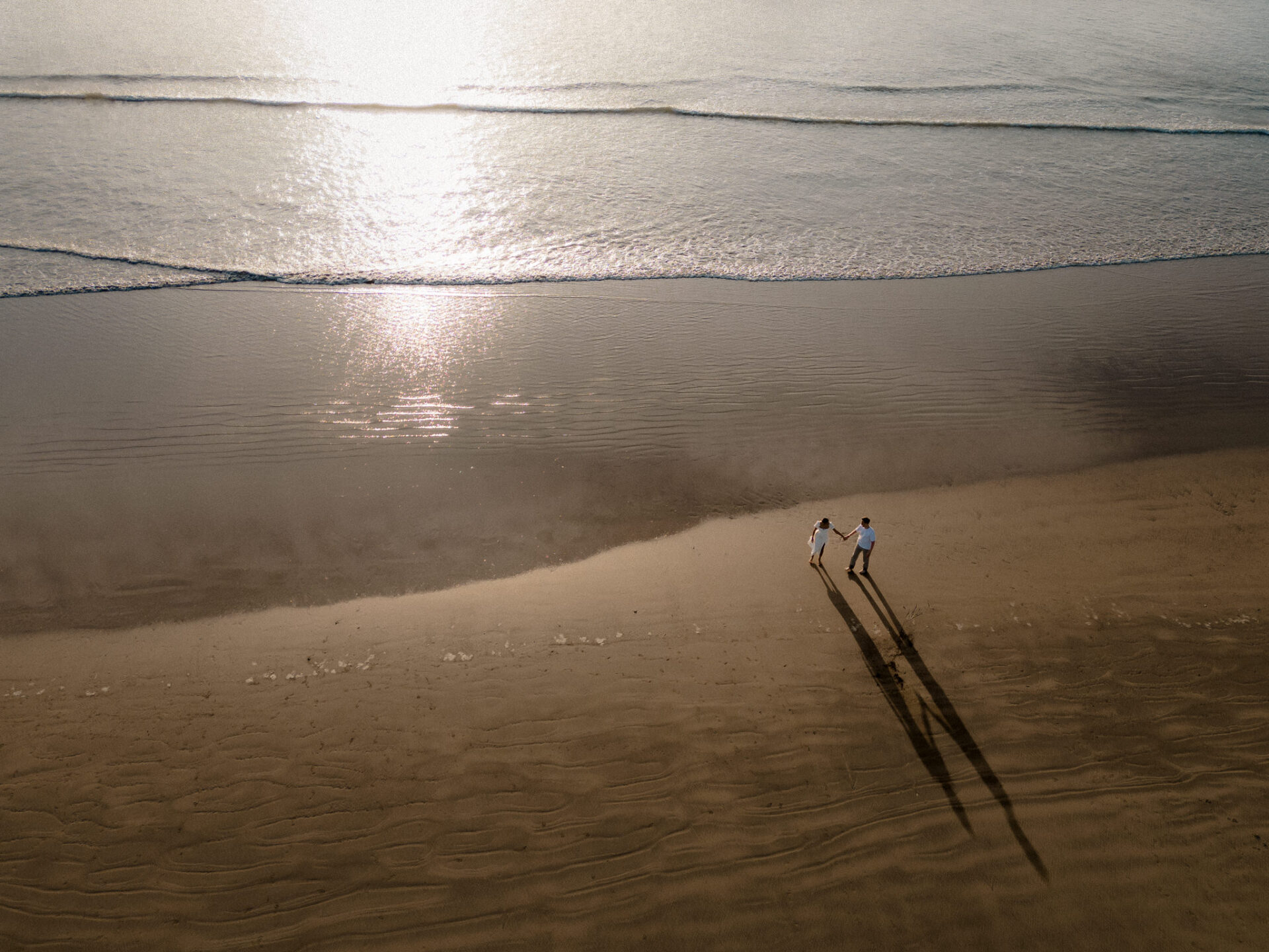 Two people walking on the beach at sunset.