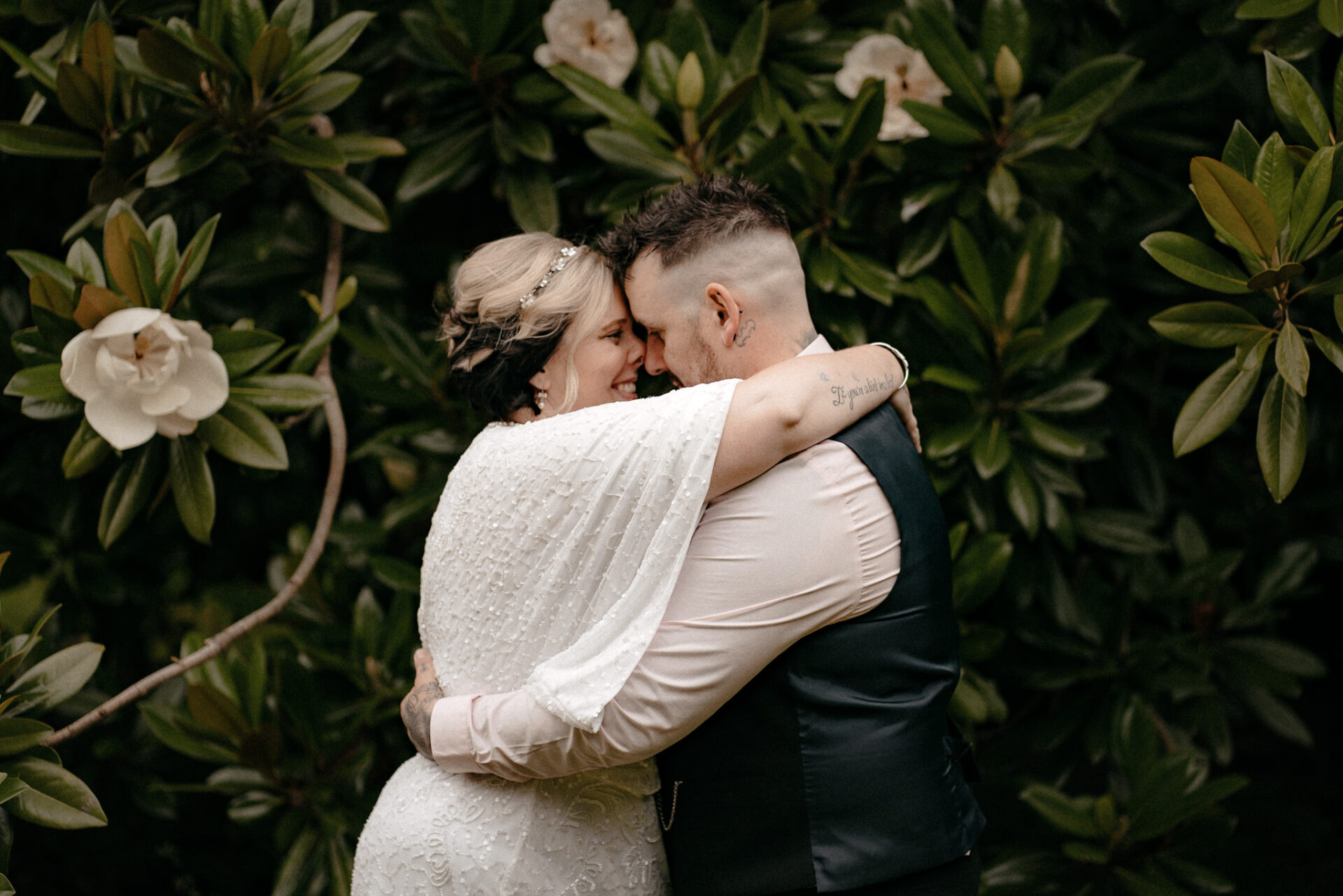 A journal documenting recent wedding stories captures a beautiful moment of a bride and groom hugging in front of bushes.