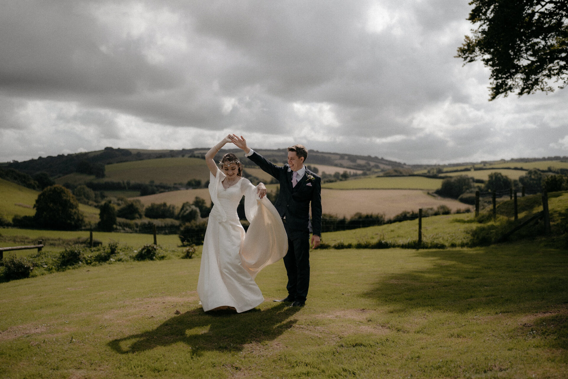 A recent wedding of a bride and groom captured in a field under a cloudy sky.