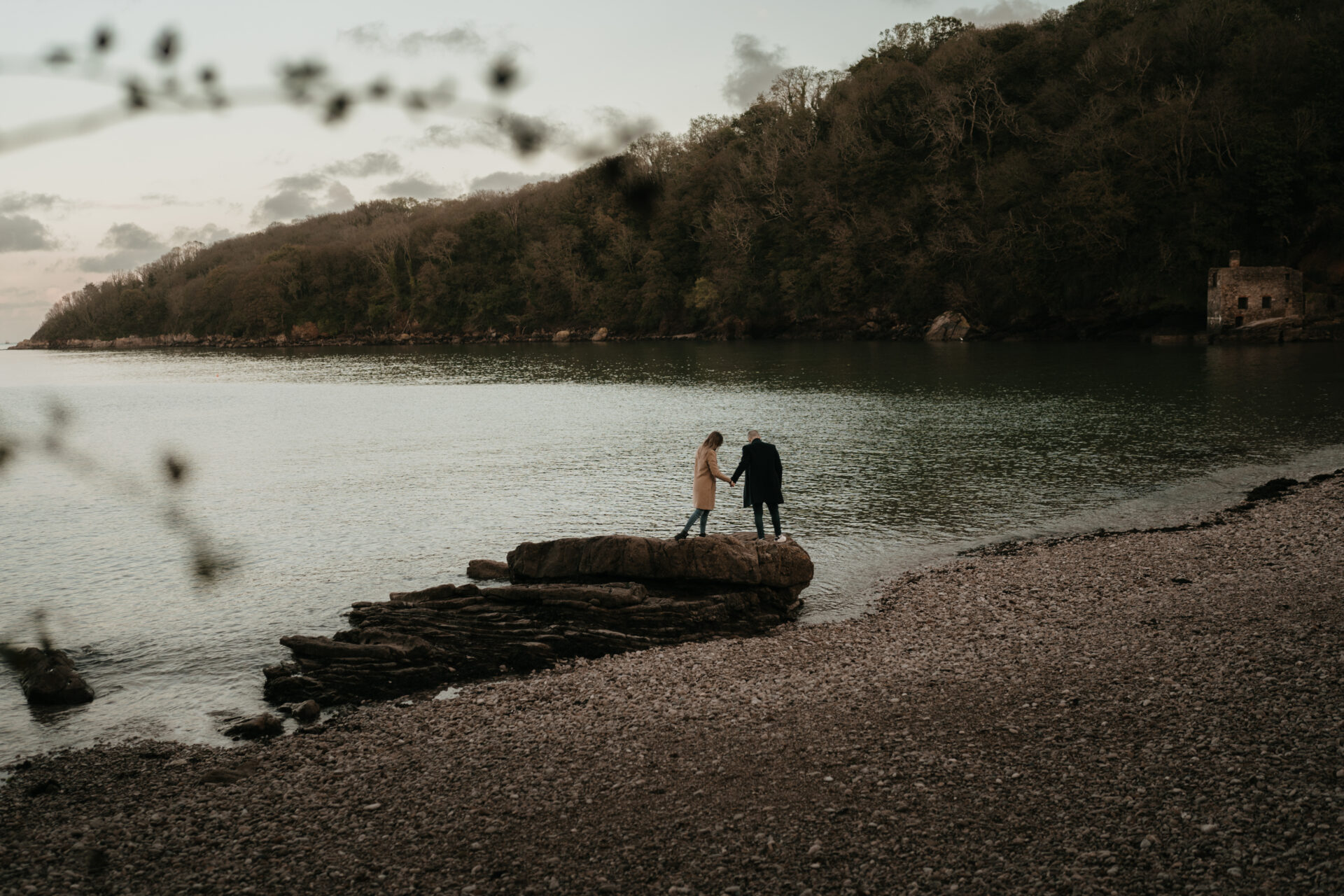 A couple standing on a rock near the water.